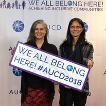 two women holding a poster that says we all belong