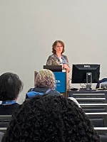 Photo of a white woman presenting in front of a group of people